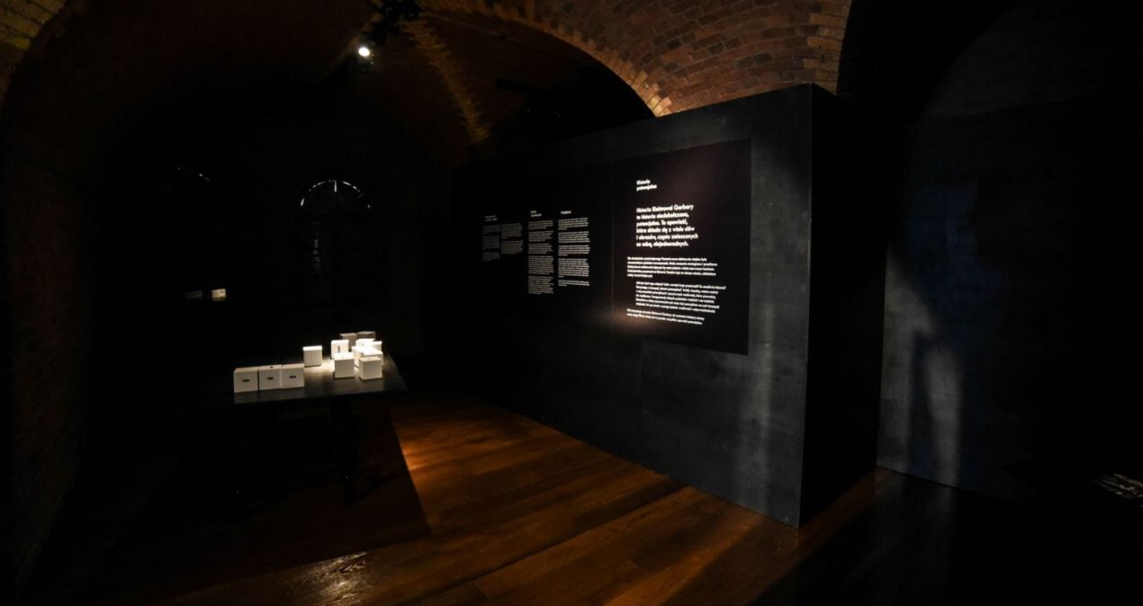 Sala wystawienicza, pośrodku stoi stół z ułóżonymi na nim białymi kostkami z czarnymi napisami