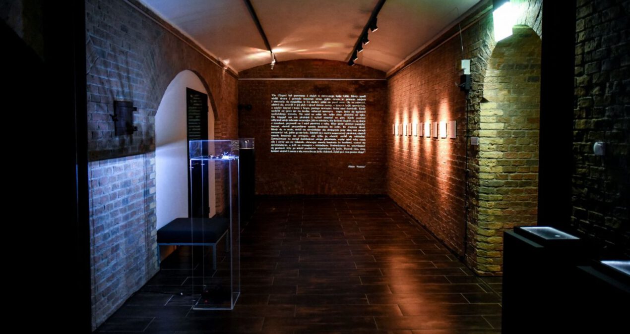 Sala wystawowa o ceglanych ścianach, na ścianie w głębi wyświetlany jest tekst