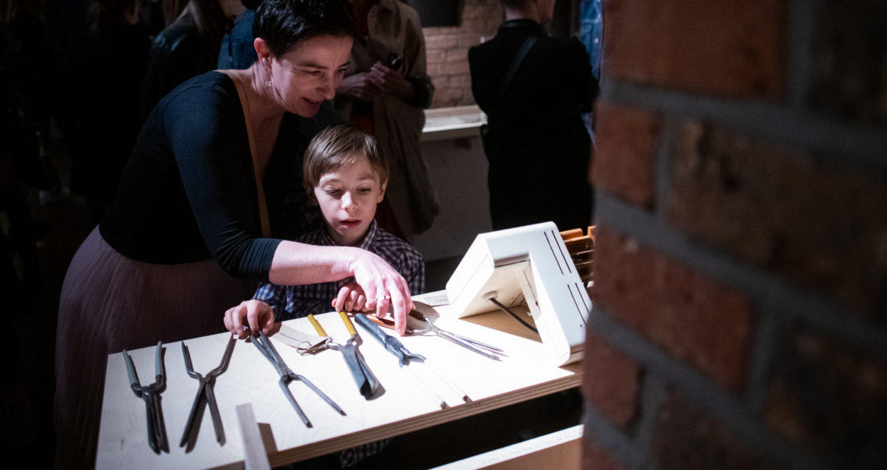 Kobieta i chłopiec przyglądają się narzędziom do kręcenia loków prezentowanym na wystawie/