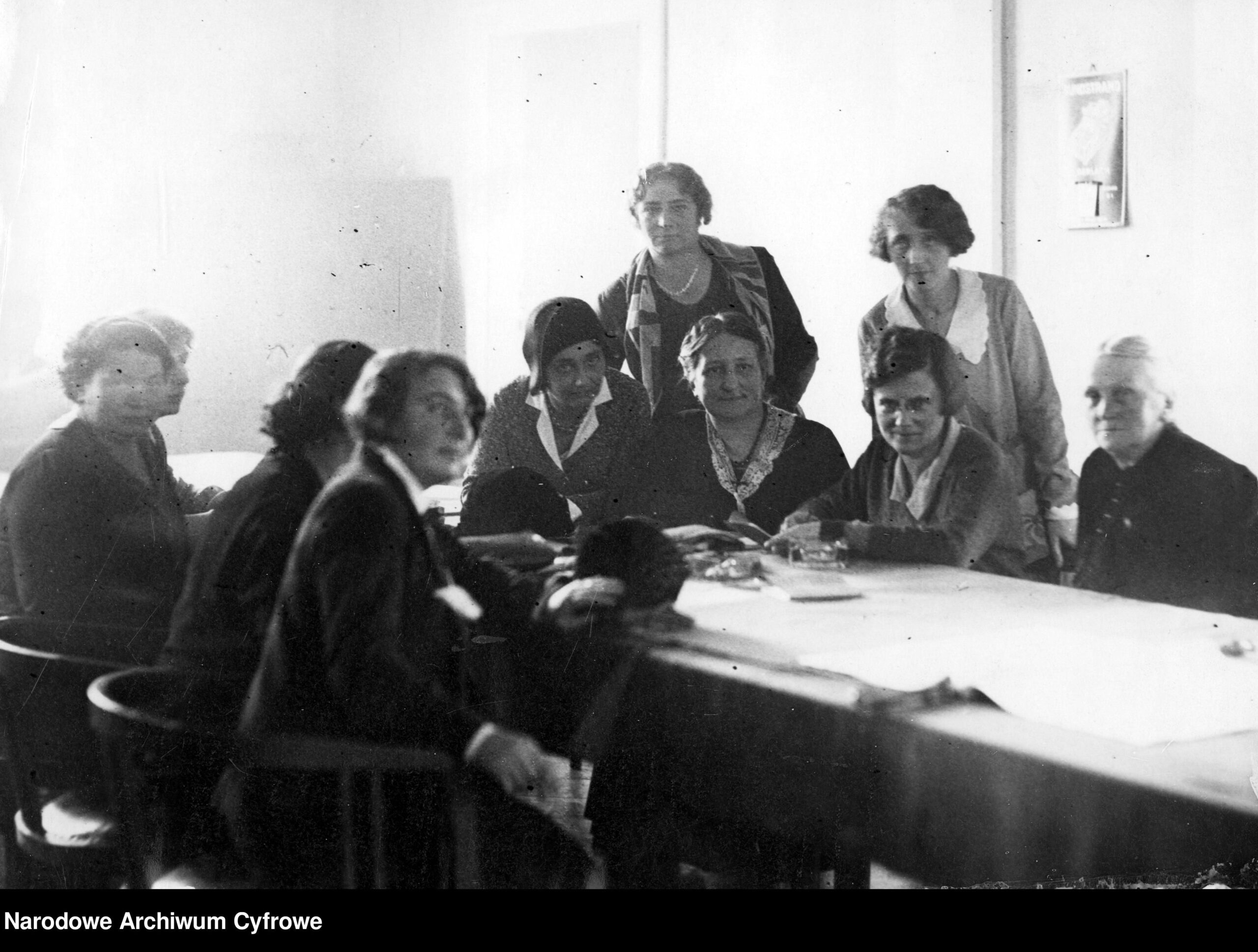Grupa kobiet zgromadzona wokół stołu. To pierwsze polskie posłanki.
